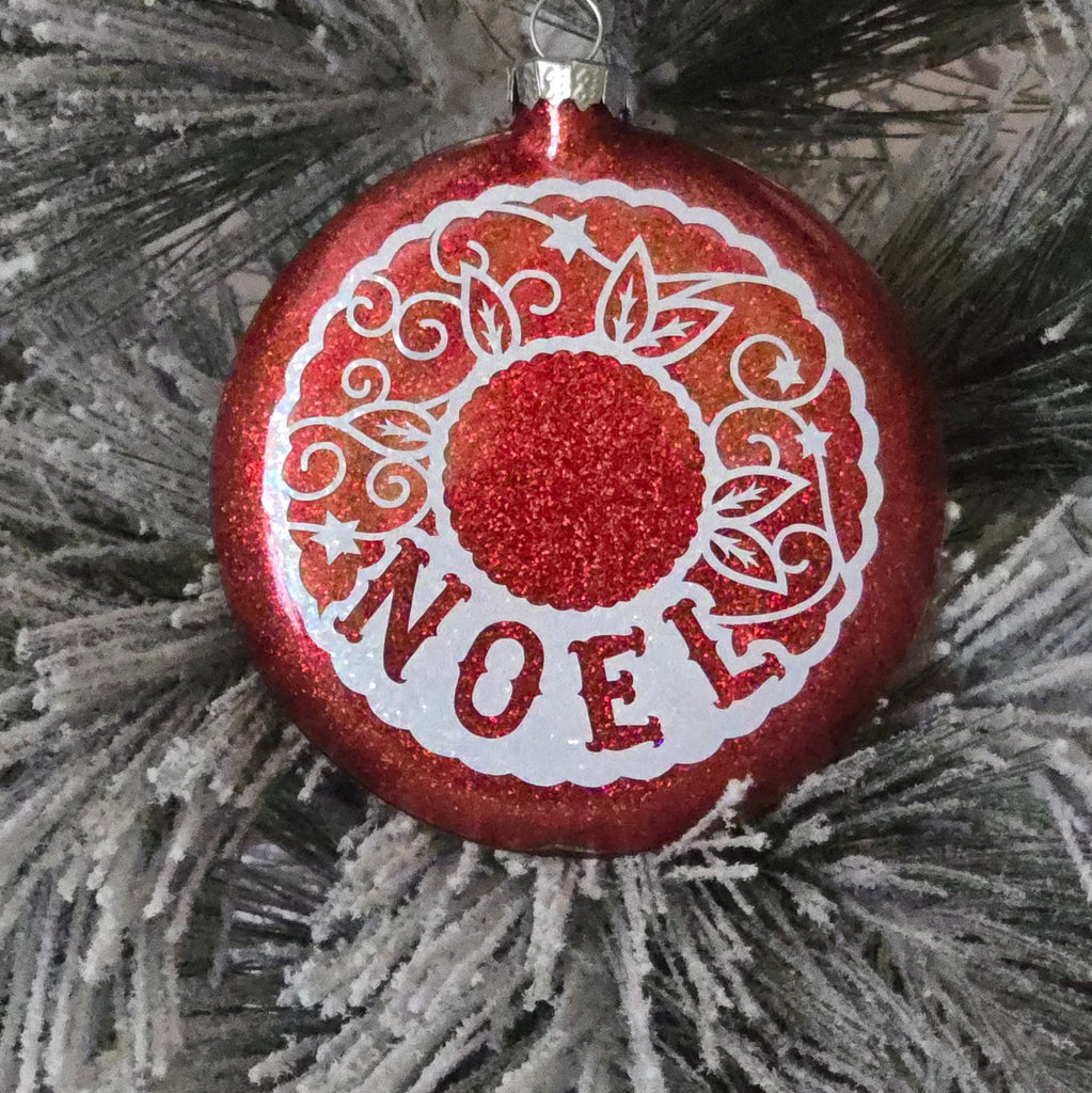 Red decorative ornament with white text on a gray pine branch