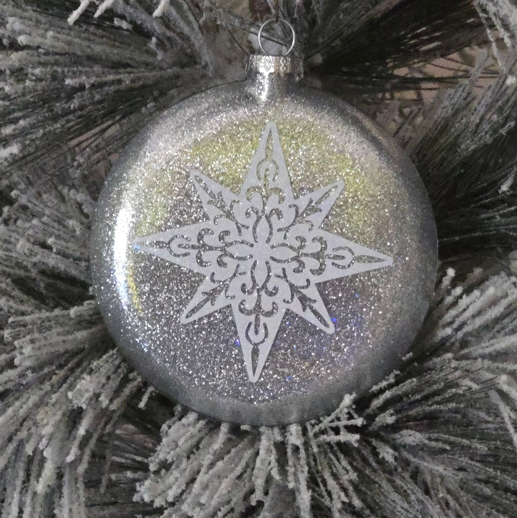 Silver Christmas ornament with snowflake design on a frosted branch
